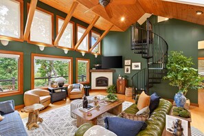 Ein geräumiges Wohnzimmer mit Kamin, großen Fenstern, einer Wendeltreppe und einer gemütlichen Sitzecke.