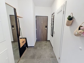 A narrow hallway with a wooden door, a mirror, a wall-mounted plant, and a small basket with flowers.