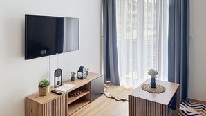 Un salon moderne avec un téléviseur à écran plat, des meubles en bois, une petite plante et un objet décoratif posé sur une table d’appoint.
