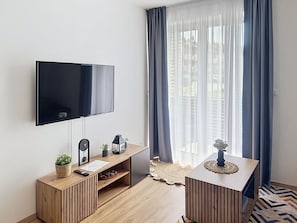 A modern living room with a flat-screen TV, wooden furniture, a small plant, and a decorative item on a side table.