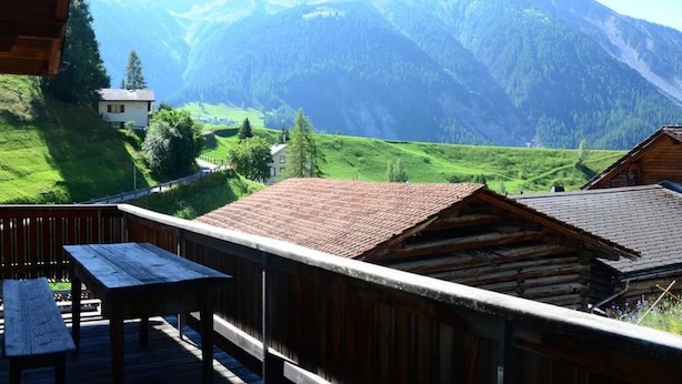 A wooden deck with a table and benches, overlooking a mountainous landscape with a house and greenery. - Obergasse Ferienhaus, Dusche oder Bad, WC Ferienhaus by Interhome (Wiesen)
