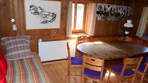 A wooden room with a bed, a table with chairs, a radiator, and wall art. - Obergasse Ferienhaus, Dusche oder Bad, WC Ferienhaus by Interhome (Wiesen)