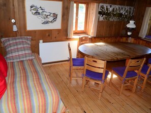 Ein Zimmer mit Holzboden, einem Bett, einem Tisch mit Stühlen, einem Heizkörper und Wandbildern.