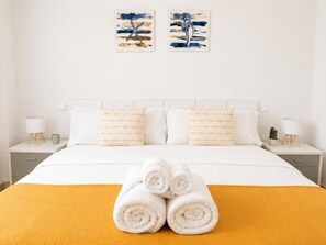Une chambre d’hôtel avec un lit, deux tables de chevet, une lampe et une serviette enroulée posée sur le lit.