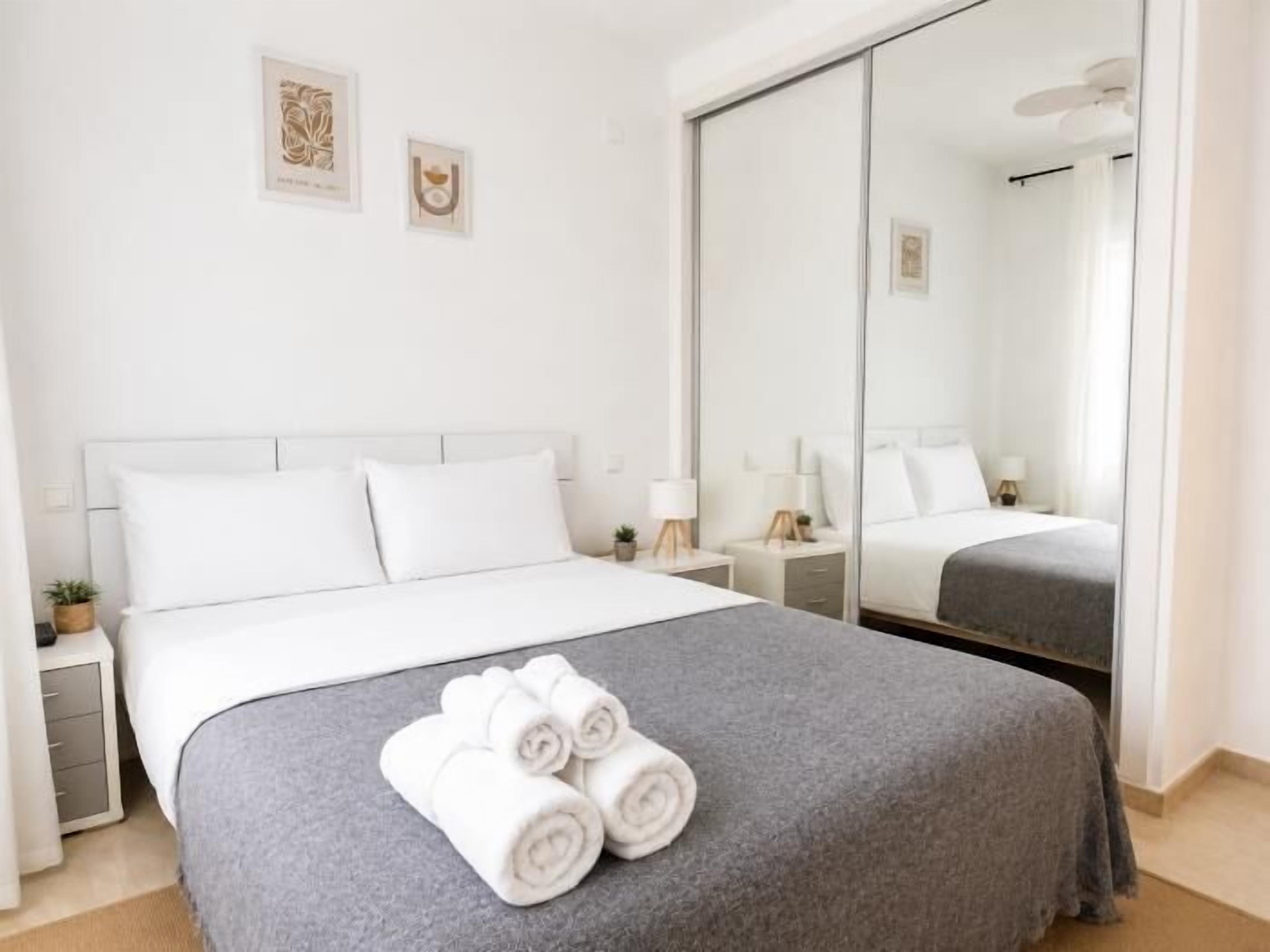 A hotel room with a bed, a nightstand, a mirror, and a wall with two framed pictures.