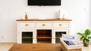 Una habitación con una mesa de madera, un armario blanco con cajones, un televisor montado en la pared mostrando 'NETFLIX' y un cartel de bienvenida sobre el armario.