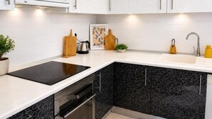 Una cocina moderna con armarios blancos, protector contra salpicaduras negro, horno empotrado y un lavamanos.