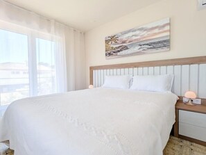 A bedroom with a large bed, a headboard, a nightstand with a lamp, and a painting of a beach scene. - Villa Rübezahl + Independent Apartment (Benidorm)