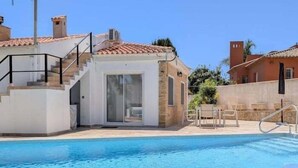 Une piscine avec une table et des chaises en verre, un verre de jus d’orange et un magazine.