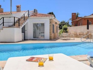 A swimming pool with a glass table and chairs, a glass of orange juice, and a magazine.