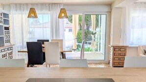 Une pièce moderne comprenant une table à manger, des chaises, un ordinateur portable et offrant une vue sur l’extérieur grâce à de grandes fenêtres.