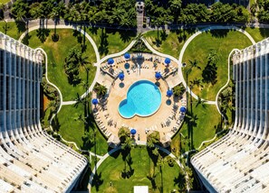 A high-rise hotel with a central swimming pool, surrounded by sun loungers and palm trees. - Luxury Beach Resort Marco Island Condo Ocean Views Pool Beach (Marco Island)