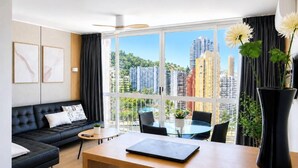 A modern living room with a sofa, a dining table, and a large window offering a city view. - Apartment with sea views in Playmon Park (Benidorm)