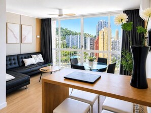 A modern living room with a sofa, a dining table, and a large window offering a city view. - Apartment with sea views in Playmon Park (Benidorm)