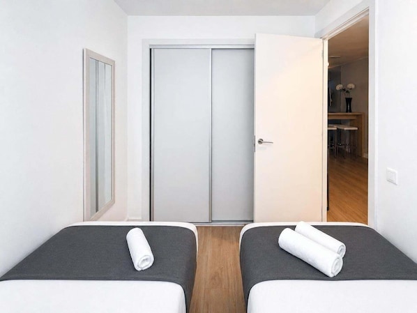 Ein Hotelzimmer mit zwei Betten, einem Kleiderschrank und einem Essbereich, der durch eine offene Tür sichtbar ist.