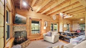 A log cabin interior with a stone fireplace, a television, a clock, and a cozy seating area. - Blue Mt. Ridge Cabin with Long Range Views, Hot Tub & Fire Pit Fun near Parkway! (Watauga County)