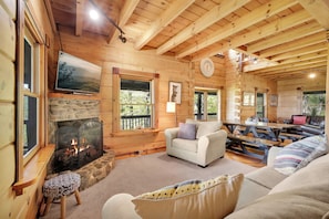 A log cabin interior with a stone fireplace, a television, a clock, and a cozy seating area. - Blue Mt. Ridge Cabin with Long Range Views, Hot Tub & Fire Pit Fun near Parkway! (Watauga County)