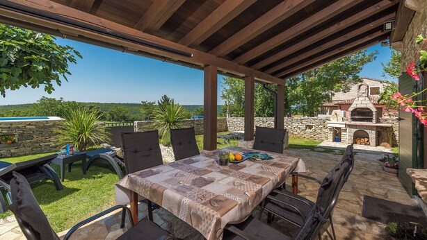 An outdoor patio with a table and chairs, a stone wall, and a view of a stone building in the background. - Villa Ana Rita (Kanfanar)