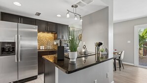 A modern kitchen with stainless steel appliances, a central island, and a dining area with a view. - The Stirrup | New | Near Old Town + Pools (Scottsdale)