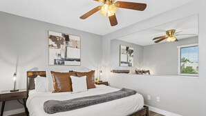 A bedroom with a bed, two nightstands, a ceiling fan, and artwork on the walls. - The Stirrup | New | Near Old Town + Pools (Scottsdale)