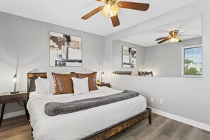 Ein Schlafzimmer mit einem Bett, zwei Nachttischen, einem Deckenventilator und Bildern an den Wänden.