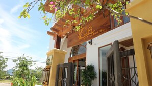 Entrada de un hotel con una pérgola de madera, un letrero que dice 'BOUTIQUE HOTEL' y un acceso con portón.
