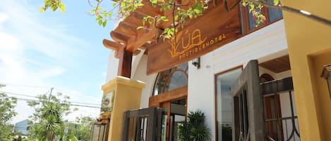 A hotel entrance with a wooden pergola, a sign reading 'BOUTIQUE HOTEL,' and a gated entrance.