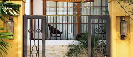 A boutique hotel entrance with a wooden pergola, a sign above the door, and a gate.