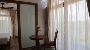 Una habitación con una cama, una mesa redonda con un florero, una silla, un ventilador de techo y cortinas traslúcidas.