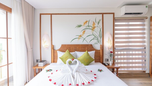 Una habitación de hotel con cama, mesita de noche, aire acondicionado instalado en la pared y ventana con persianas.