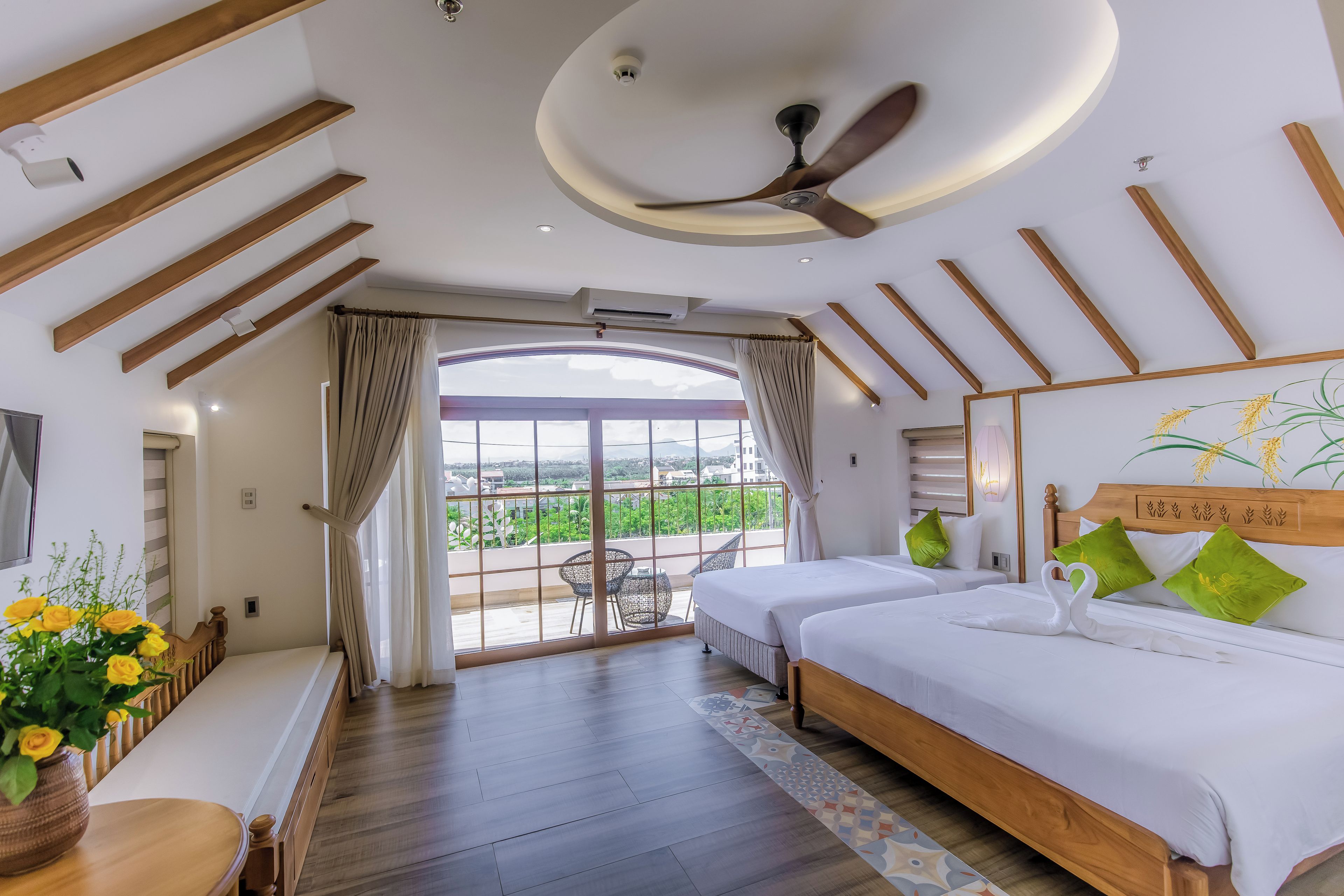 A hotel room with a balcony, two beds, a ceiling fan, and a view of the outdoors.