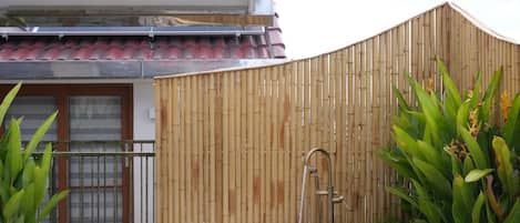 Ein großer Außenwhirlpool auf einer Holzterrasse mit Bambuszaun und Topfpflanzen.