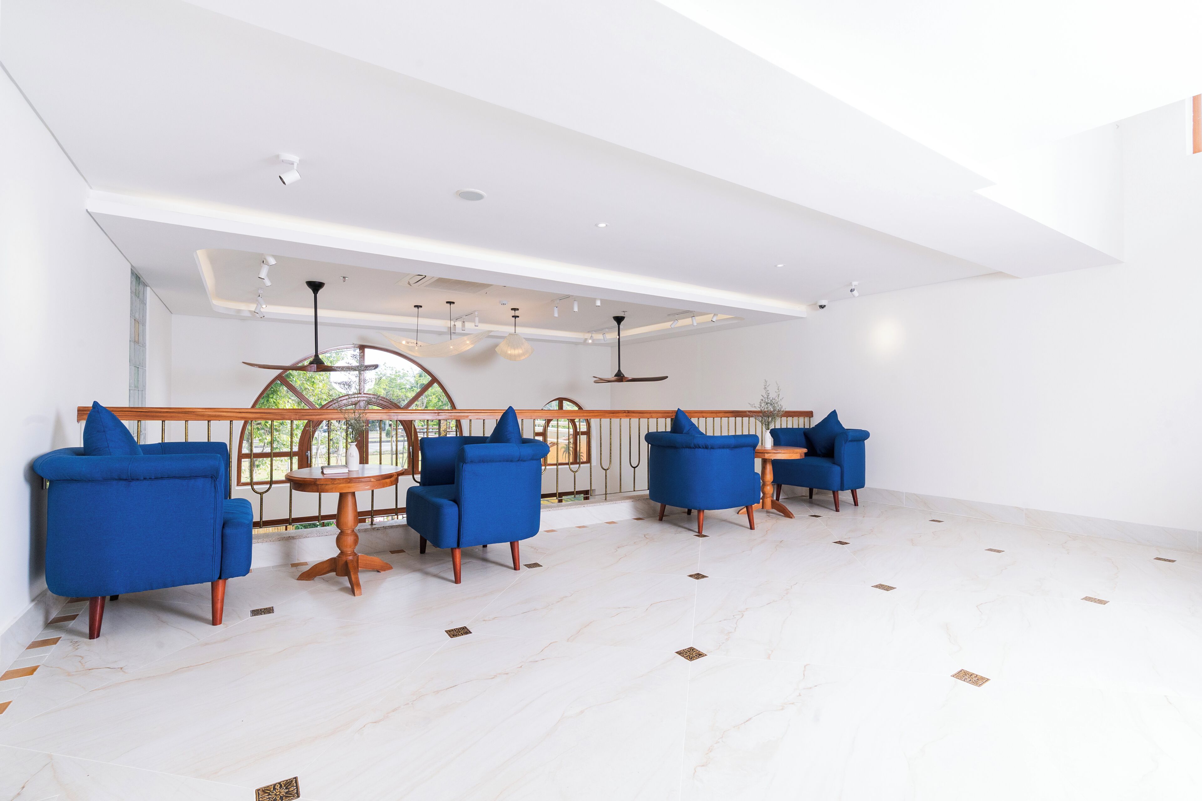 A spacious room with a high ceiling, white walls, and a large window. There are three blue armchairs and a wooden table.