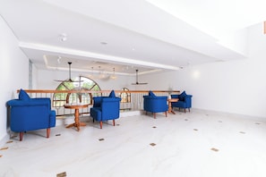 A spacious room with a high ceiling, white walls, and a large window. There are three blue armchairs and a wooden table. - Lua Boutique Hotel & Spa - An Bang Beach (Da Nang)