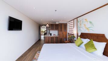 A bedroom with a bed, a TV mounted on the wall, and a kitchen area in the background.