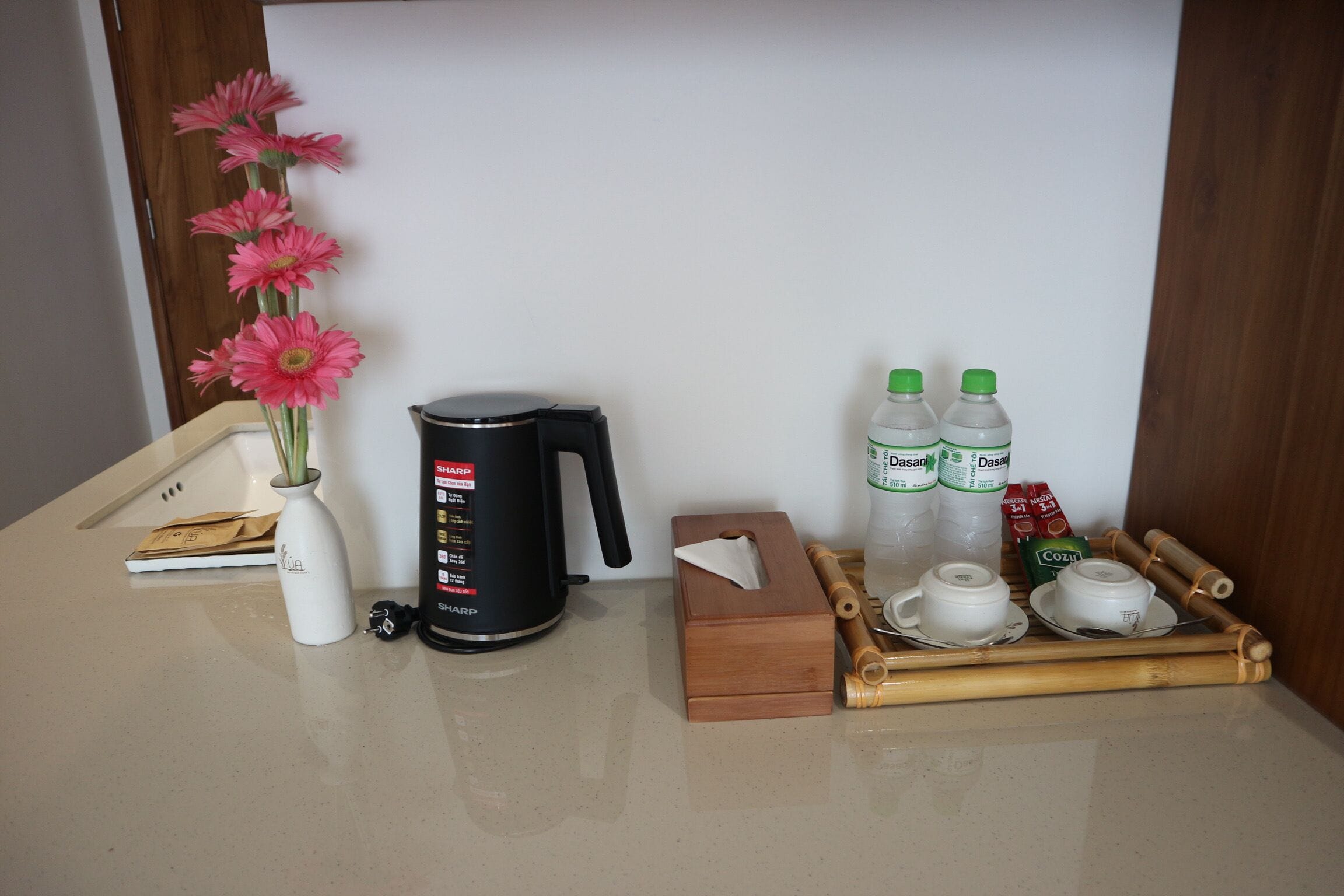 A kitchen counter with a coffee maker, a vase with flowers, a tissue box, and a tray with cups and bottles.