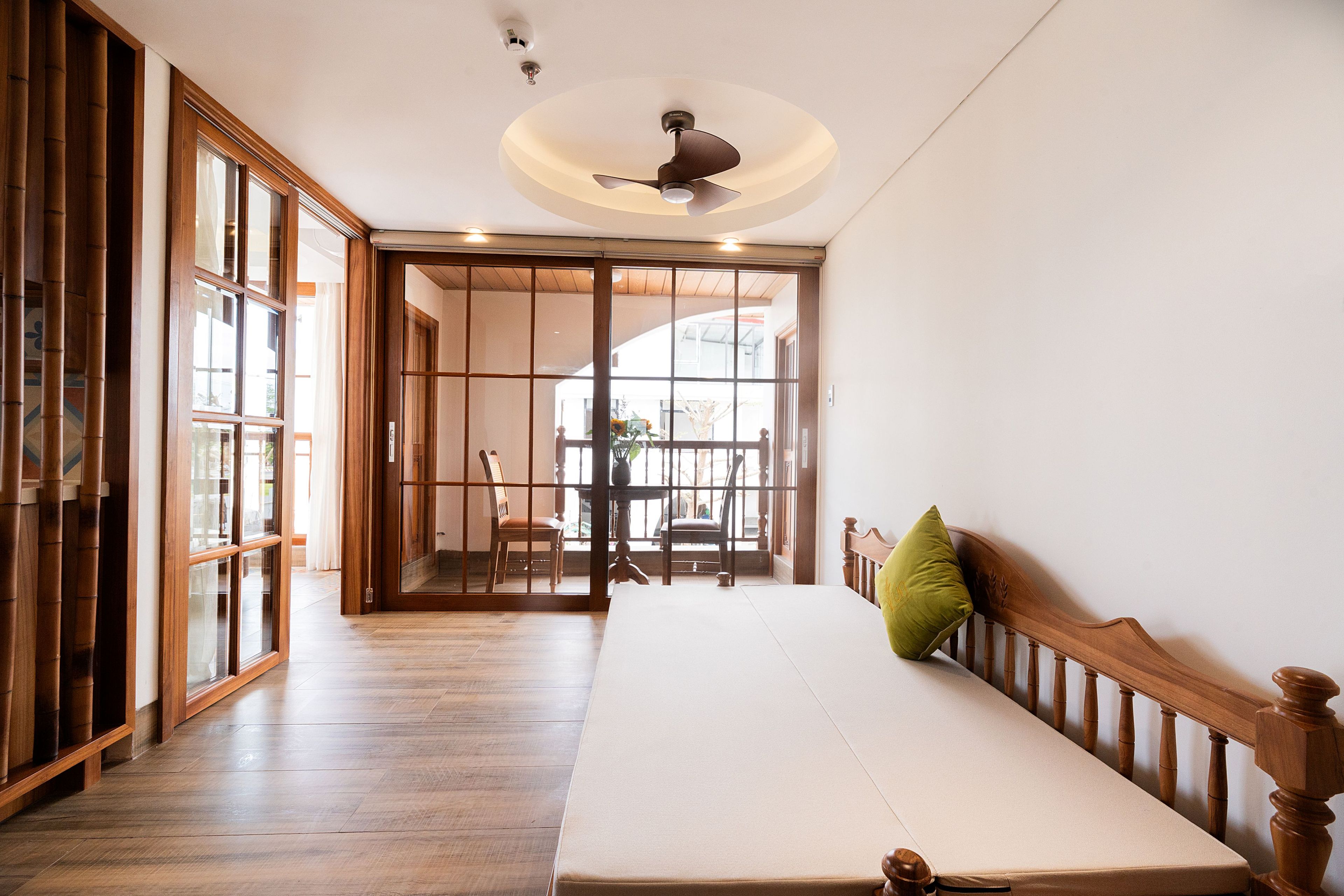 A room with a wooden floor, a bed with a pillow, a ceiling fan, and a sliding door leading to another room.