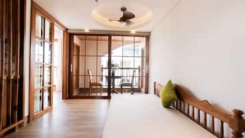 A room with a wooden floor, a bed with a pillow, a ceiling fan, and a sliding door leading to another room.