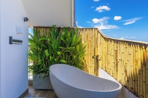 Un baño moderno con una bañera independiente, una valla de bambú y vistas al cielo.