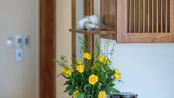 Un baño con un mueble de madera, un lavabo blanco, un jarrón con flores amarillas y una tetera negra.