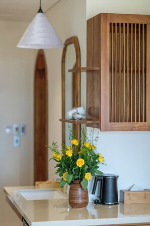 A bathroom with a wooden cabinet, a white sink, a vase with yellow flowers, and a black kettle. - Lua Boutique Hotel & Spa - An Bang Beach (Da Nang)