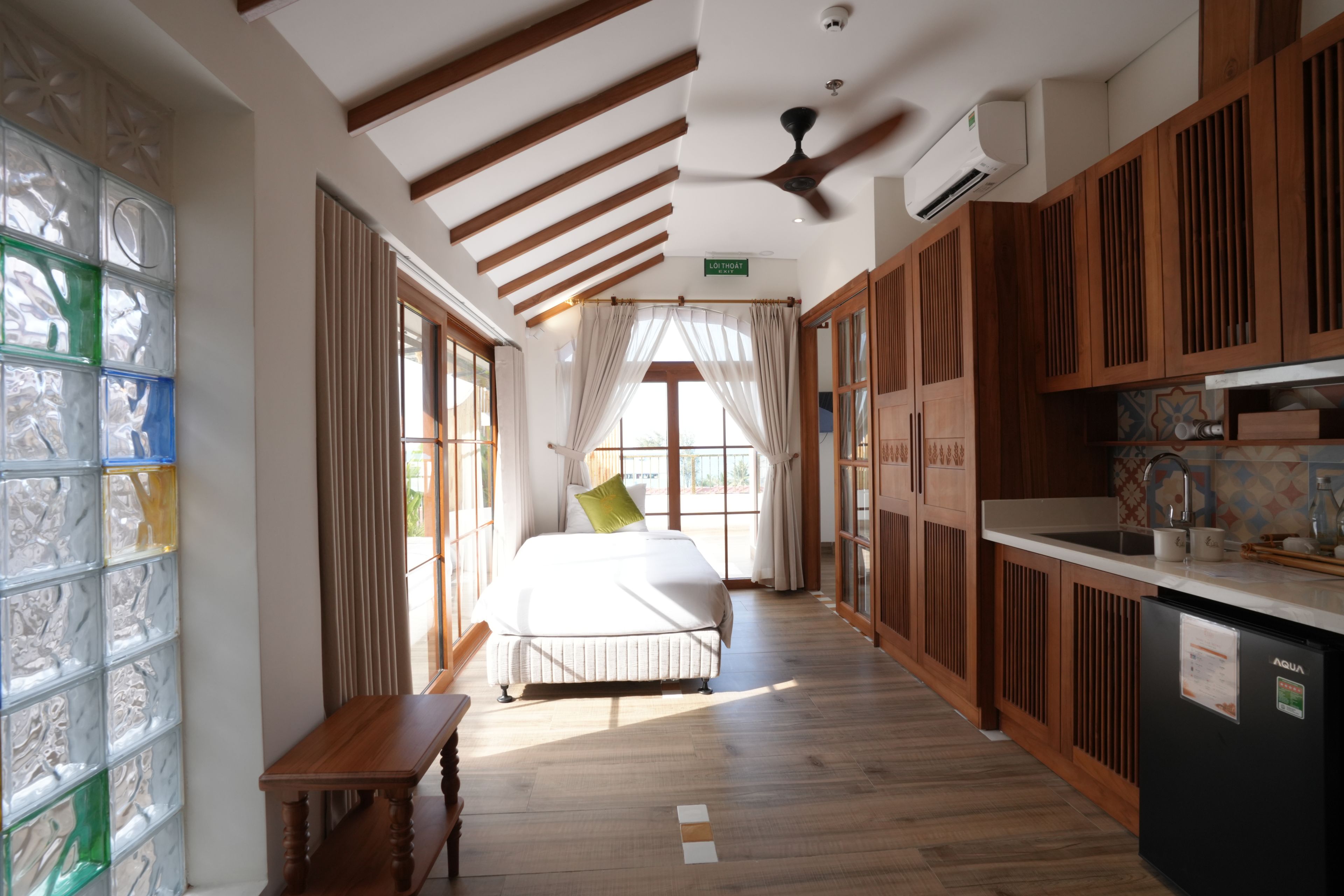A hotel room with a bed, a bench, a dining table, and a kitchen area.