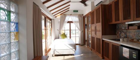 A hotel room with a bed, a bench, a dining table, and a kitchen area.