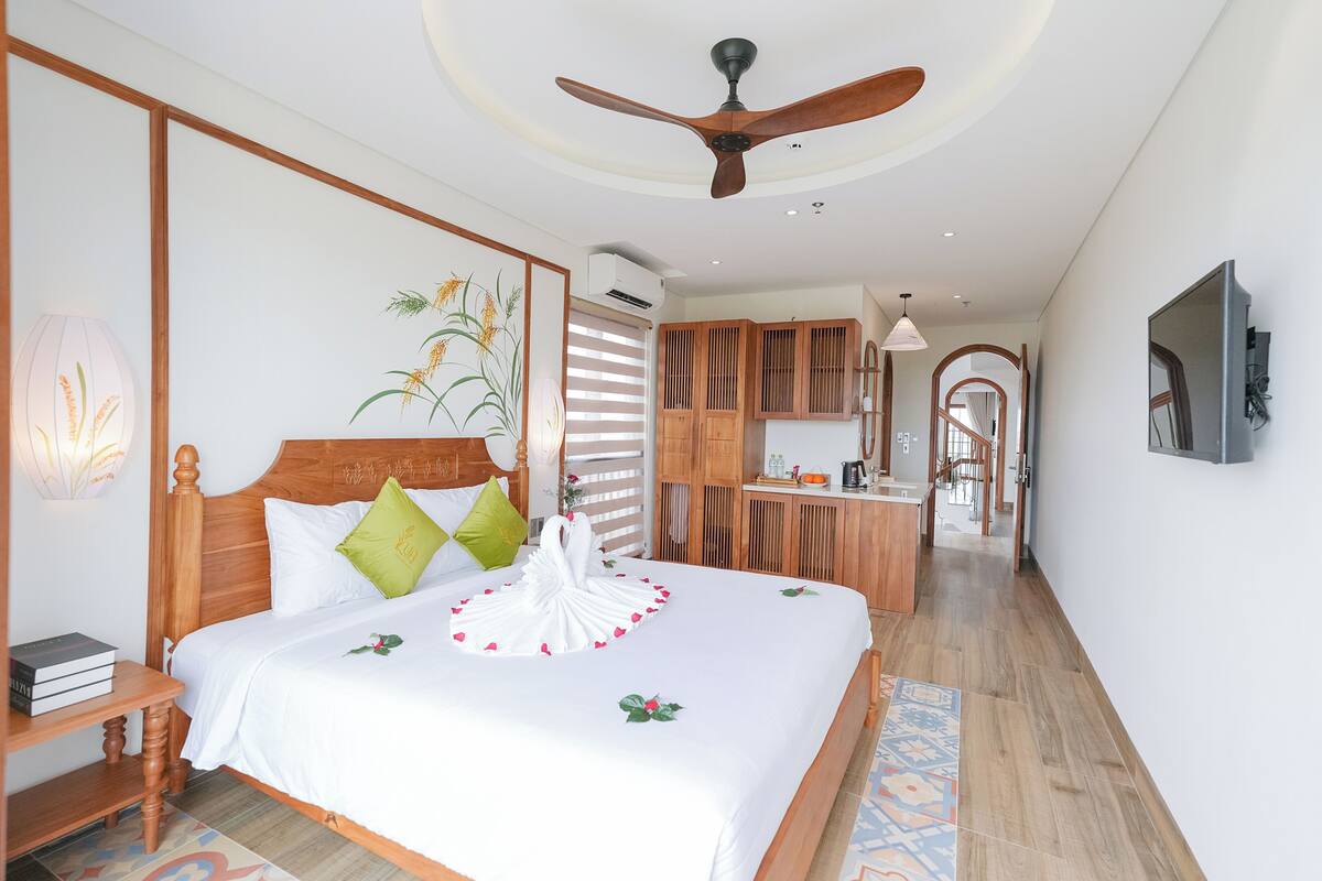 Una habitación de hotel con una cama de madera, un ventilador de techo, un armario de madera, un escritorio y un baño con ducha.