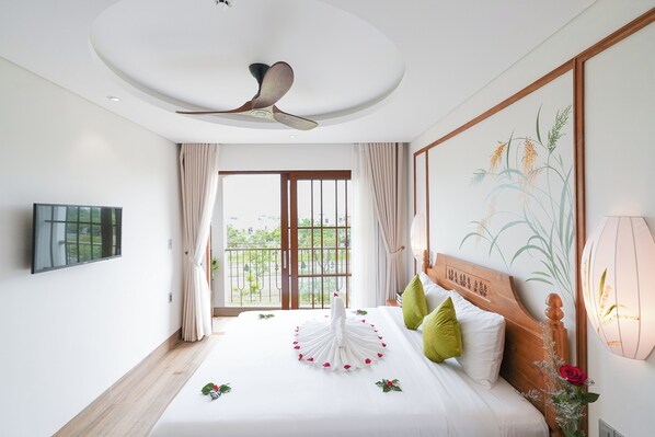 A hotel room with a bed, a ceiling fan, a TV, a window with curtains, and a wall-mounted light fixture. - Lua Boutique Hotel & Spa - An Bang Beach (Da Nang)