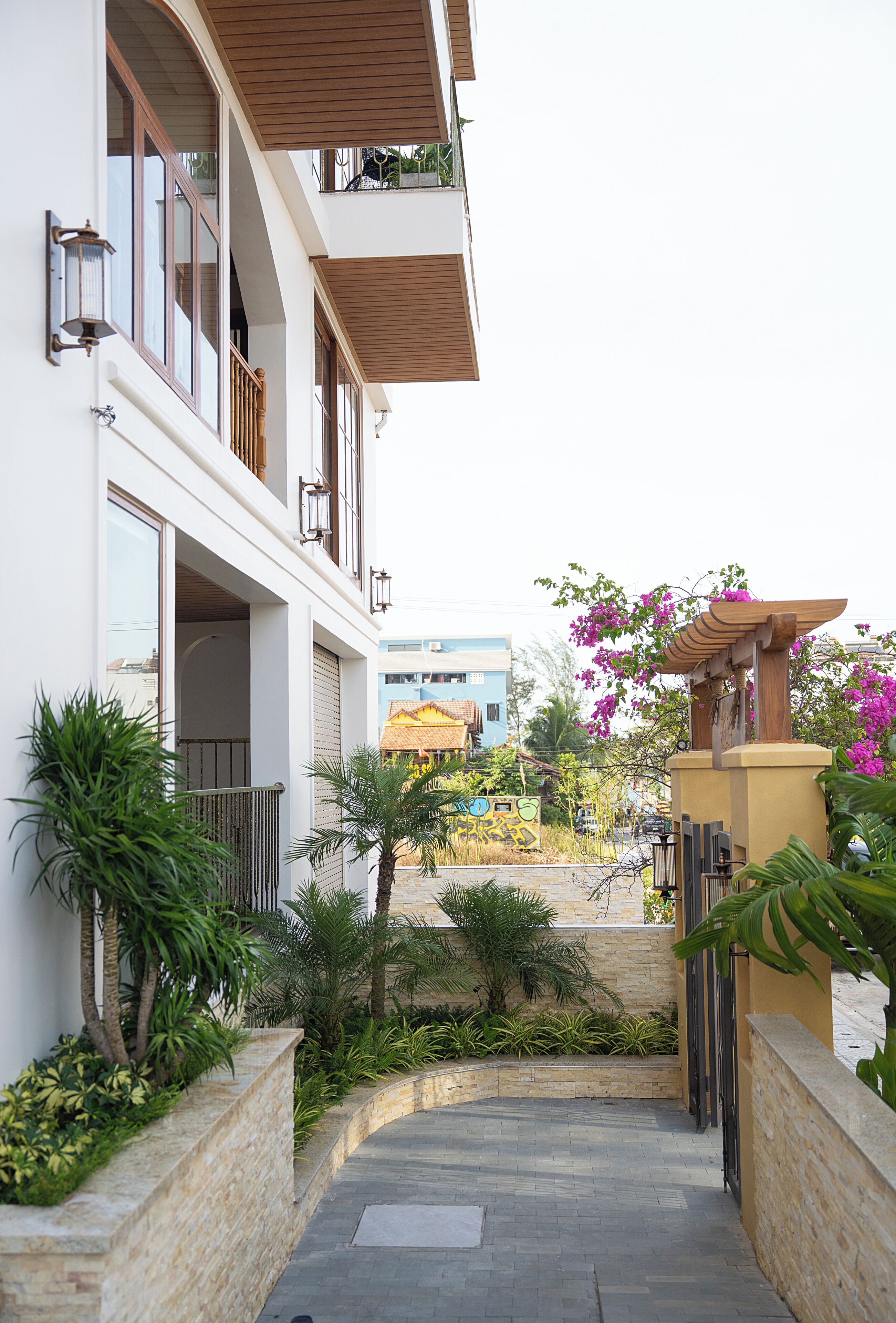 Un edificio de varios pisos con balcones, un camino pavimentado y abundante vegetación.