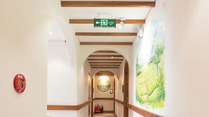 Un pasillo de hotel con suelo de madera, un extintor y un letrero de salida verde.