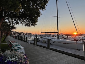 Ein Yachthafen bei Sonnenuntergang mit vertäuten Booten, einer Holzpromenade und einer Reihe von Bänken.