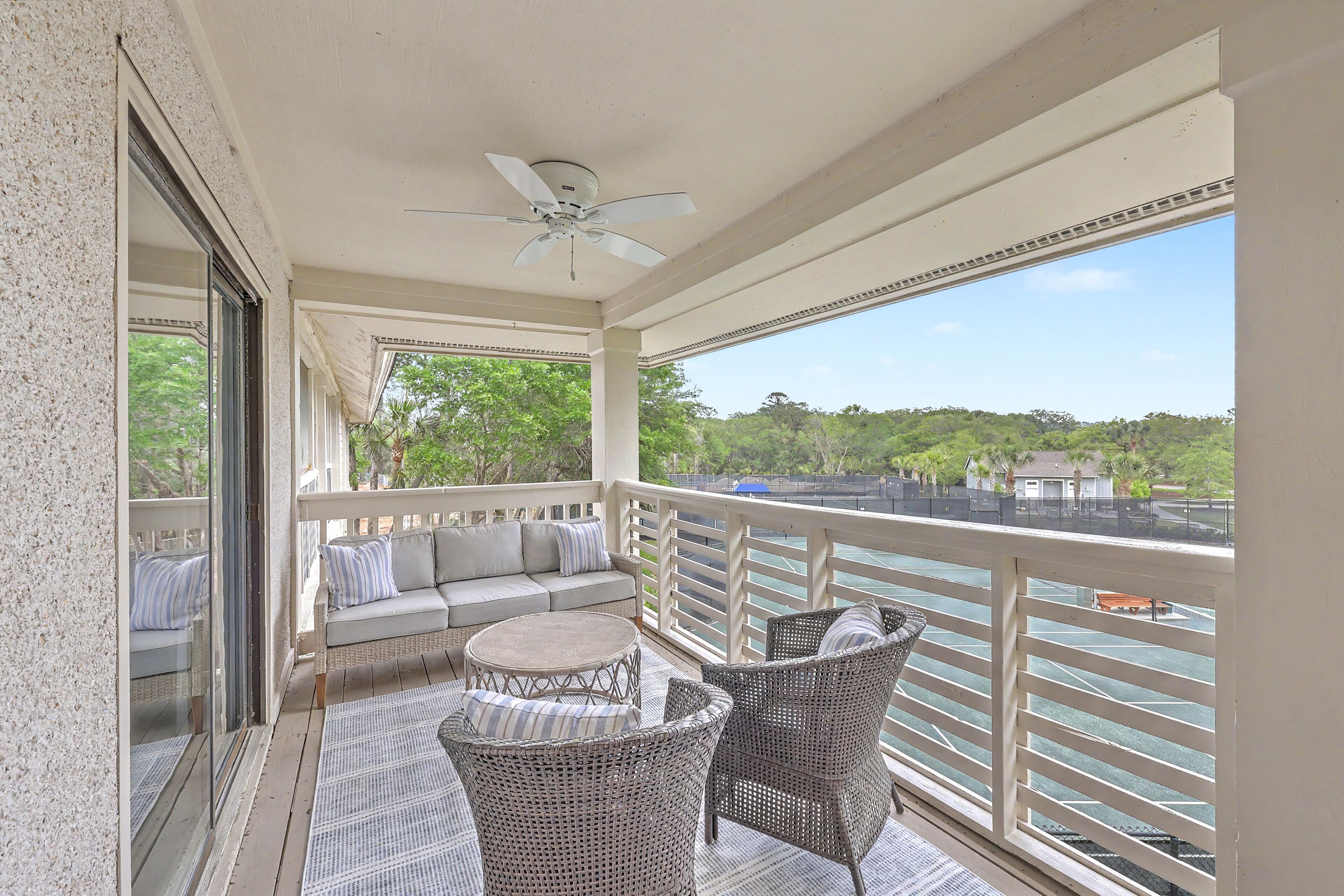 A balcony with a sofa, chairs, a table, and a ceiling fan.