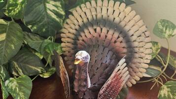 Una figurita de pavo con un abanico de palitos de madera, rodeada de plantas de hojas verdes.